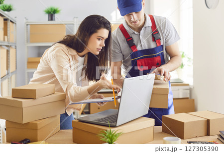 Woman with colleague standing at workplace in storeroom checking stock and inventory on laptop Woman with colleague standing at workplace in storeroom checking stock and inventory on laptop 127305390