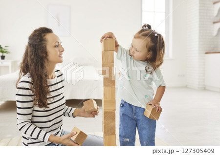 Happy Daughter Playing With Wooden Toys Alongside Her Mother At Home 127305409