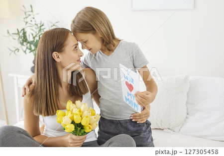 Loving son embracing his mother, giving her handmade card and tulips for Mother Day or Women Day. Loving son embracing his mother, giving her handmade card and tulips for Mother Day or Women Day. 127305458
