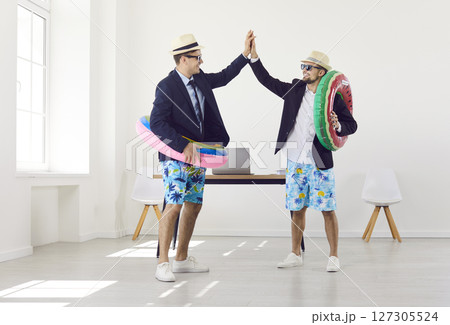Funny workers standing in office with rubber ring giving high five going on holiday trip. Funny workers standing in office with rubber ring giving high five going on holiday trip. 127305524