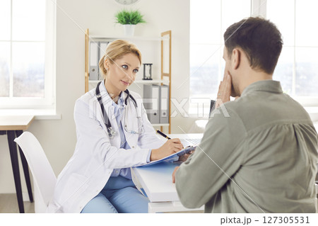 Young female doctor listening man patient sitting in office during medical examination. Young female doctor listening man patient sitting in office during medical examination. 127305531