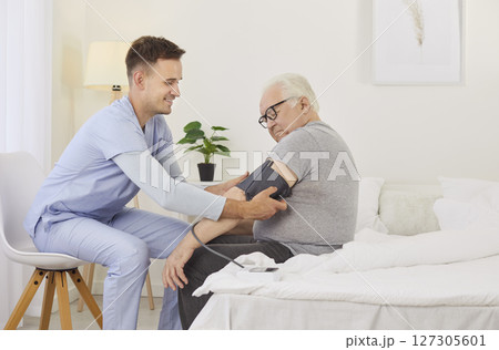Blood pressure measured, nurse brother helping sick senior man sitting on medical couch at home 127305601