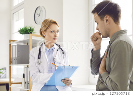 Young careful doctor female medical worker in uniform listening to unhealthy male patient at clinic 127305718