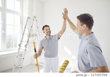 Painters holding paint rollers and giving high five after successful job finishing painting Painters holding paint rollers and giving high five after successful job finishing painting 127305769