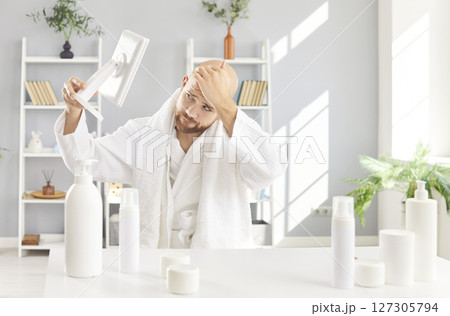 Man In Bathrobe Looking At Bald Head In Mirror Man In Bathrobe Looking At Bald Head In Mirror 127305794