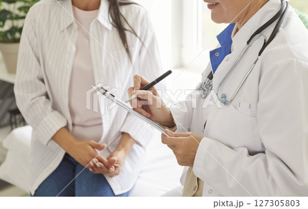 Close up female doctor holding clipboard, filling patient form, documents, medical history  127305803