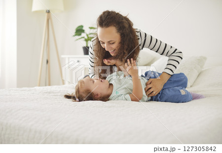 Happy, loving mother cuddling and tickling her little child daughter on the bed at home 127305842