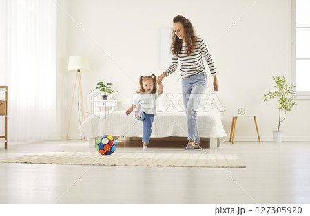 Happy young mother holding hands with preschool daughter playing football and kicking colorful ball. Happy young mother holding hands with preschool daughter playing football and kicking colorful ball. 127305920