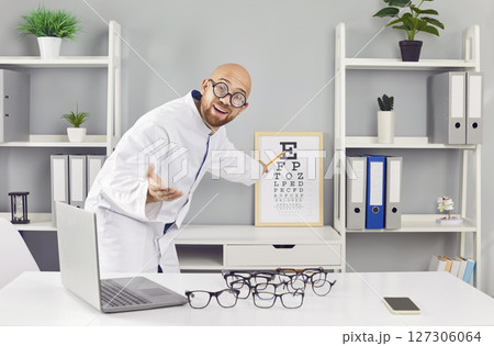 Funny optician male doctor checking a patient's vision at desk in ophthalmology clinic. 127306064