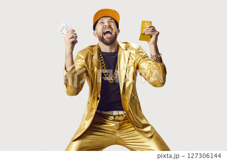 Shocked funny man in golden suit holding money cash and gold bar on white studio background. 127306144