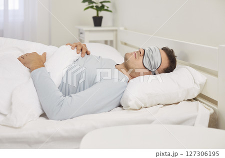 Man Sleeping In Bed At Home Early In The Morning Wearing A Sleep Mask Man Sleeping In Bed At Home Early In The Morning Wearing A Sleep Mask 127306195