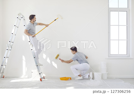 Professional team of house painters holding paint rollers and painting the wall of new apartment. 127306256