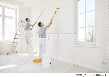 Male painters or construction workers painting walls in white color with paint roller brush Male painters or construction workers painting walls in white color with paint roller brush 127306271