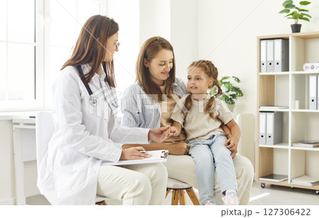 Pediatrician talking to mother and little girl during visit, offering support during health checkup. Pediatrician talking to mother and little girl during visit, offering support during health checkup. 127306422