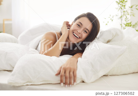 Relaxed happy brunette woman lying in bed under white blanket, enjoying peaceful morning at home. Relaxed happy brunette woman lying in bed under white blanket, enjoying peaceful morning at home. 127306502