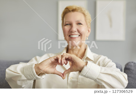Elderly Woman Sitting At Home Showing Heart Sign With Hands 127306529