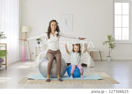 Mother sitting on fit ball with child daughter and doing sport exercises at home together 127306625