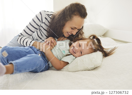 Loving young mother and her daughter sharing joyful moments in sunlit bedroom, playing and laughing. Loving young mother and her daughter sharing joyful moments in sunlit bedroom, playing and laughing. 127306732
