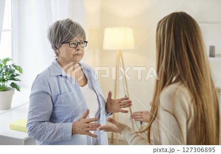 Unhappy elderly mother gesturing during conflict and misunderstandings with her adult daughter. 127306895