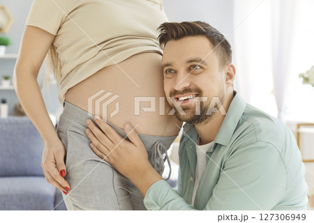 Happy smiling excited expectant father cuddling his wife pregnant belly, listening to baby moving. 127306949