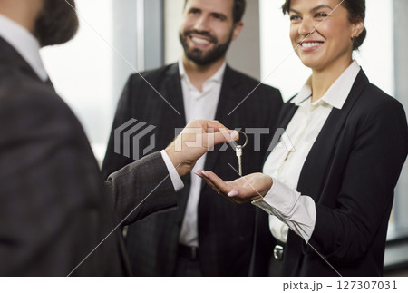 Smiling businesswoman receiving key from partner after deal, symbolizing ownership transfer. Smiling businesswoman receiving key from partner after deal, symbolizing ownership transfer. 127307031