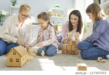 Happy women and children sitting on carpet and playing with wooden toys during creative family time. Happy women and children sitting on carpet and playing with wooden toys during creative family time. 127307033