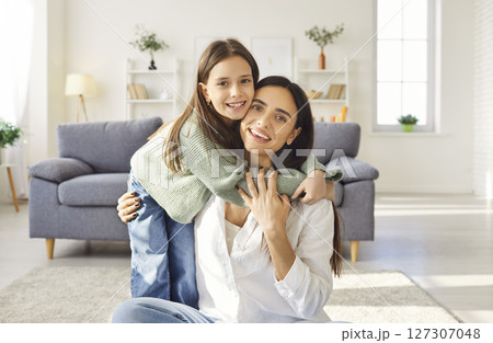 Mother and daughter portrait, loving cute little girl hugs around neck, cuddles excited young mum 127307048