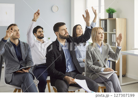 Young cheerful company employees raising hands to vote at the conference sitting in meeting room. Young cheerful company employees raising hands to vote at the conference sitting in meeting room. 127307199