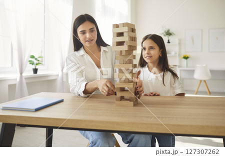 Mother sitting at table with teenage girl and playing an educational wooden building blocks at home Mother sitting at table with teenage girl and playing an educational wooden building blocks at home 127307262