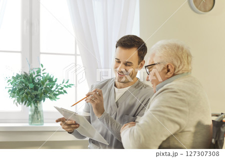 Nurse discussing treatment with senior elderly disabled man patient in wheelchair in nursing home 127307308