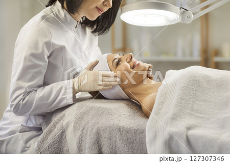 Woman cosmetologist exam young woman skin condition under lamp in beauty spa salon. 127307346