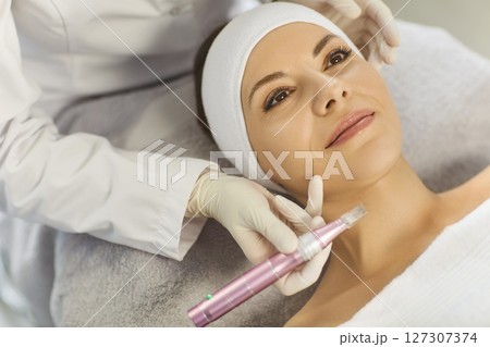 Woman receiving apparatus facial treatment procedure from cosmetologist in beauty wellness salon. 127307374