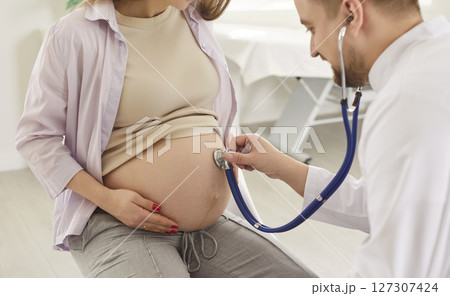Male gynecologist doctor examining young pregnant woman with stethoscope in medical clinic Male gynecologist doctor examining young pregnant woman with stethoscope in medical clinic 127307424