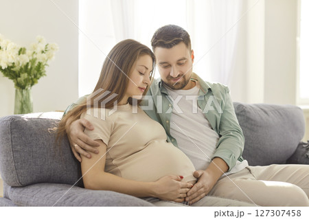Expectant Parents Touching Pregnant Belly While Relaxing On Couch At Home 127307458