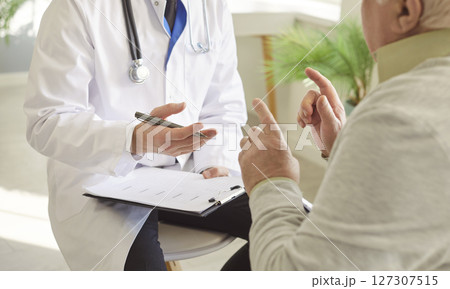 Senior sick man talking to male doctor in white uniform sitting in clinic during medical examination. 127307515