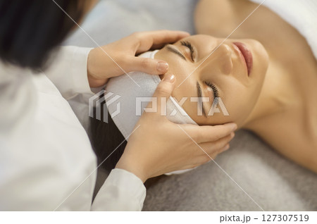 Young woman enjoying relaxing face massage during professional skincare spa treatment at spa salon. Young woman enjoying relaxing face massage during professional skincare spa treatment at spa salon. 127307519
