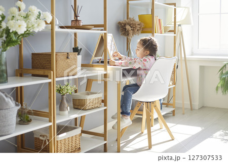 Little girl kid in modern playroom with accessories for game and study, enjoys creative hobby  127307533