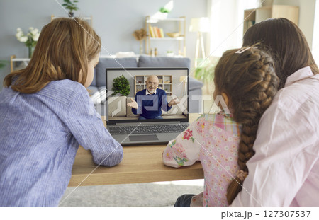 Family sitting at home and having online video call with grandfather using laptop. Family sitting at home and having online video call with grandfather using laptop. 127307537