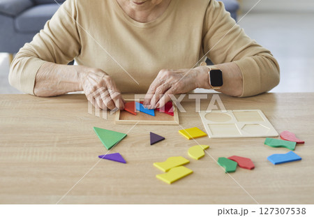 Elderly woman assembling colourful geometric shapes, developing her motor skills  127307538