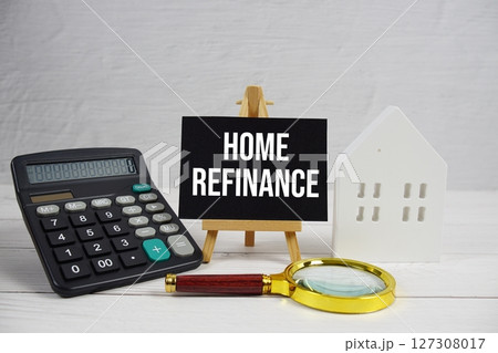Home Refinance on paper card with white house model, calculator and magnifying glass on wooden background 127308017