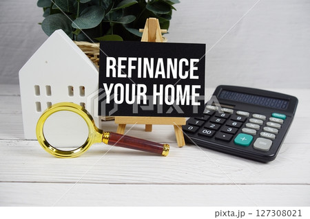 Refinance Your Home on paper card with white house model, calculator and magnifying glass on wooden background 127308021
