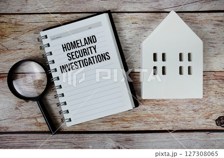 Homeland Security Investigations text on paper notebook with white house model and magnifying glass on wood background 127308065
