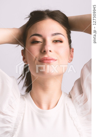 Happy woman close-up studio portrait with hands behind her head 127309945