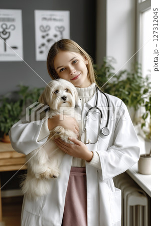 Young veterinarian trainee holding a small dog in a bright clinic with plants and artwork Young veterinarian trainee holding a small dog in a bright clinic with plants and artwork 127312045