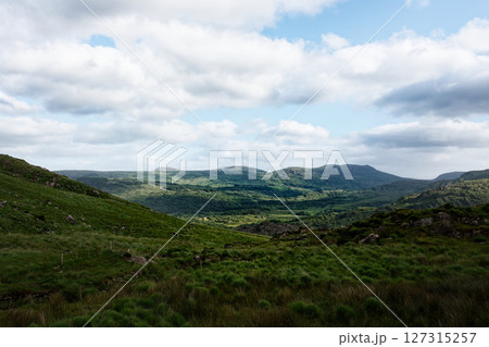 Serene Irish landscape unfolds, rolling green hills meet a bright sky. Peaceful valley bathed in sunlight. 127315257