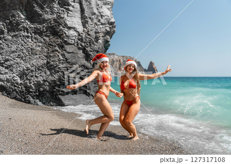 Women in Santa Claus hats run into the sea dressed in red swimsuits. Celebrating the New Year in a hot country 127317108
