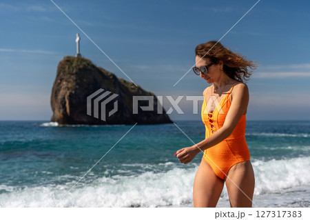 Beach Woman Swimsuit Cape Fiolent day: Lady walks on the beach wearing orange swimsuit on sunny day. 127317383