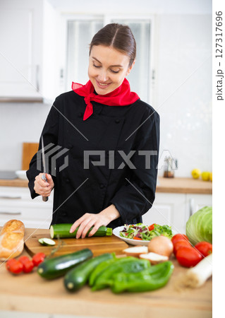 Positive woman personal chef in black uniform preparing vegetable dish Positive woman personal chef in black uniform preparing vegetable dish 127317696