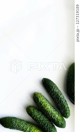 Five small cucumbers are laid out in a fan-like pattern on a clean white background, showcasing freshness and texture. 127319189
