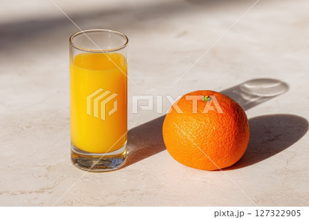 Fresh Orange Juice in Clear Glass Beside Whole Orange on Light Marble Surface 127322905